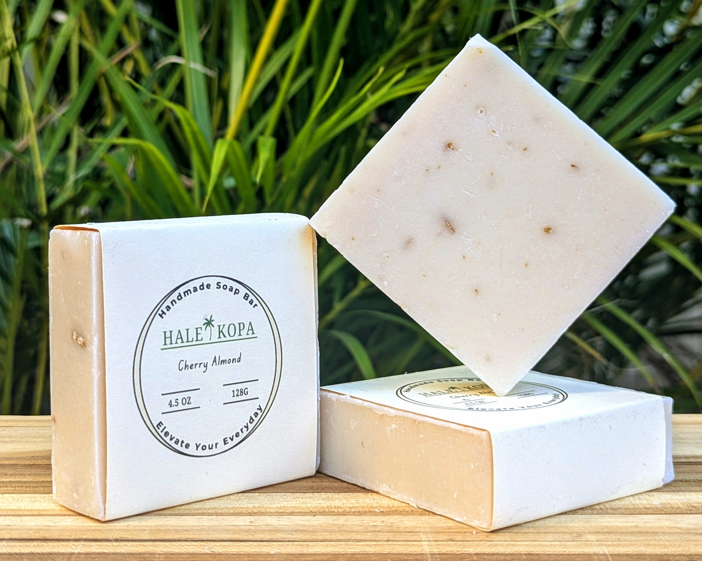 A bar of soap with a light beige color, placed on a wooden surface with a box in the background displaying the product name 'Cherry Almond'.