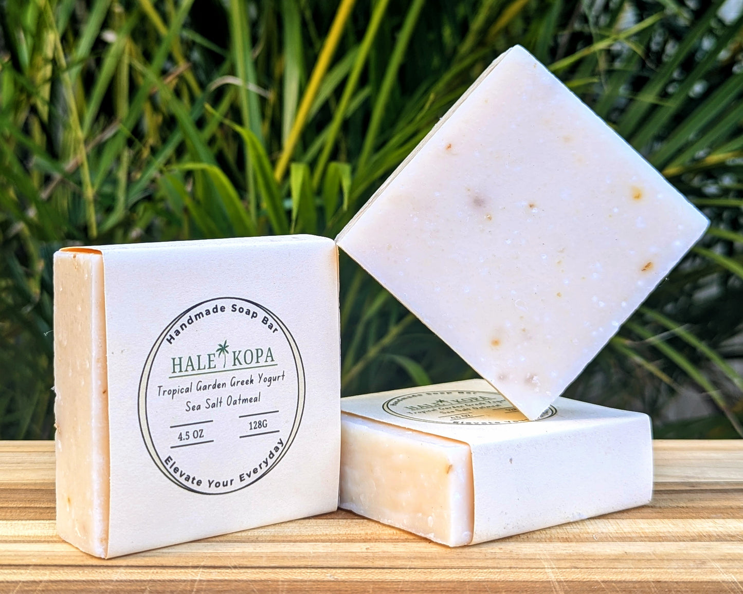 A bar of soap with a white label that reads 'Hale Kopa', 'Tropical Garden', 'Greek Yogurt', 'Sea Salt', 'Oatmeal'. The bar of soap is partially cut, revealing the light-colored oatmeal exfoliants inside.